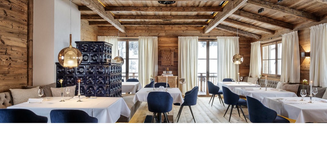 Restaurant im Hotel Severin*s – The Alpine Retreat in Lech Gemütliches Restaurant mit Holzwänden, blauen Samtstühlen, weißen Tischdecken und großen Fenstern mit Bergblick.